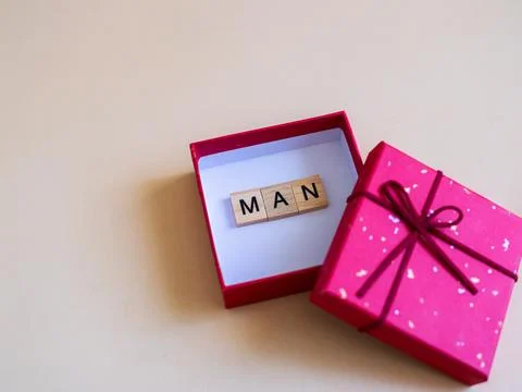 Gift box, man, letter tile, pink package with ribbon on beige background Foto stock