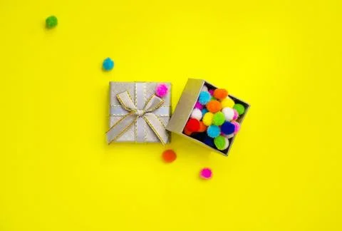 Gift box with multi-colored confetti on a yellow background. Stock Photos