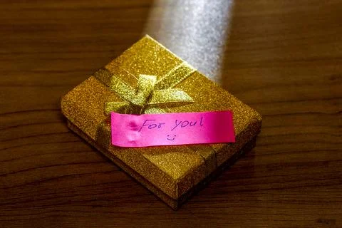 Gift box with a note on a wooden table surface. Stock Photos