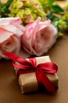 Gift box present with red bow, pink roses, brown background. Stock-Fotos