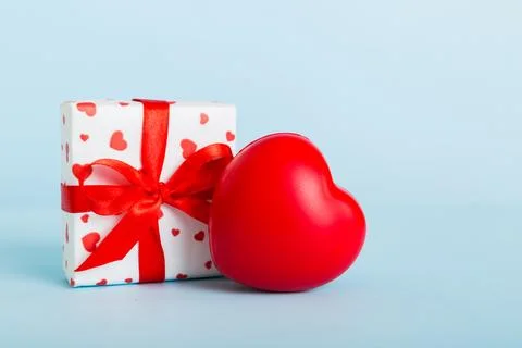 Gift box with red bow and red heart on colored background. Perspective view.. Stock Photos