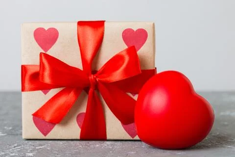 Gift box with red bow and red heart on colored background. Perspective view.. Stock Photos