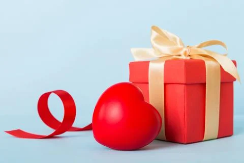 Gift box with red bow and red heart on colored background. Perspective view.. Stock Photos