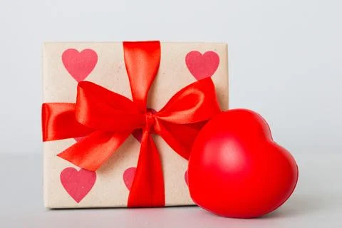 Gift box with red bow and red heart on colored background. Perspective view.. Stock Photos