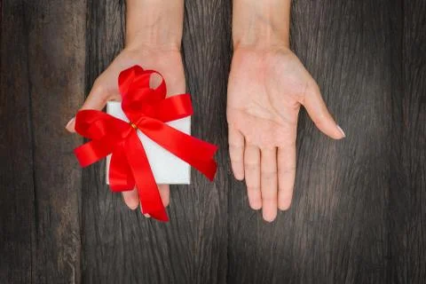 Gift box with a red bow in hand on a wooden background. Stock Photos