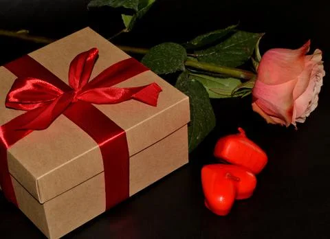 Gift box with red bow, pink rose and aroma candles on a black background. Stock-Fotos