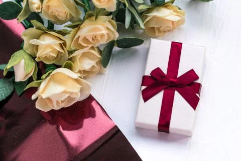 Gift box with a red bow on a table with yellow roses on a white wooden table 스톡 사진