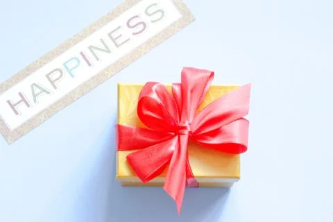 Gift box with red bow with text Happiness on a blue background. Flat lay Stock Photos