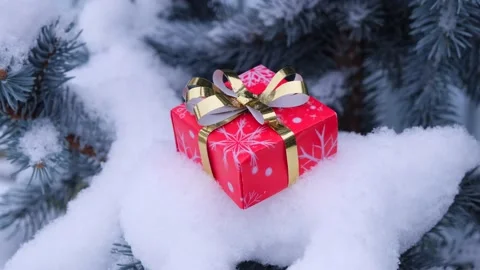 Gift box in red paper with gold bow on a branch of a Christmas tree and falling Stock Footage 167434685