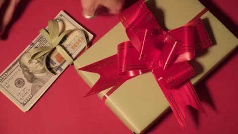 Gift box with ribbon and dollar bills on dark red background, top view. Concept Stock Footage 322542645