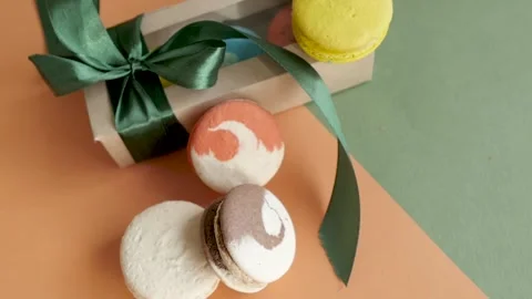 Gift box with ribbon and inside macaroni comes in a frame on green and orange Video stock 139579452