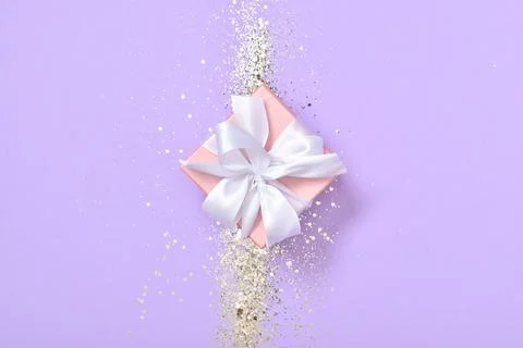 A gift box with sequins on a purple background. Minimalism. Stock Photos