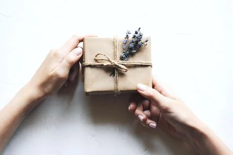 A gift box in a simple concise paper package with a bouquet of lavender in hands Stock Photos