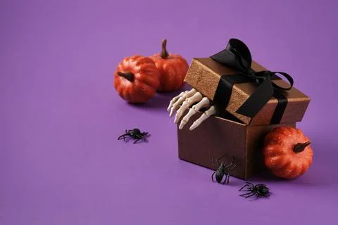 Gift box with skeleton hands, mini pumpkins and spiders on a purple backgroun Stock Photos