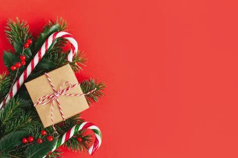 Gift box with spruce branches, red berries and candy cane on a red background Stock Photos