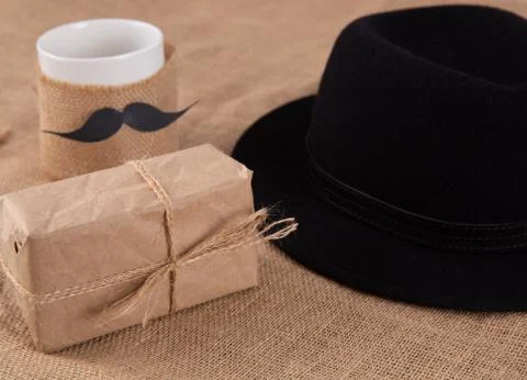 Gift box on the table. Next to a cup with a glued mustache. Stock Photos