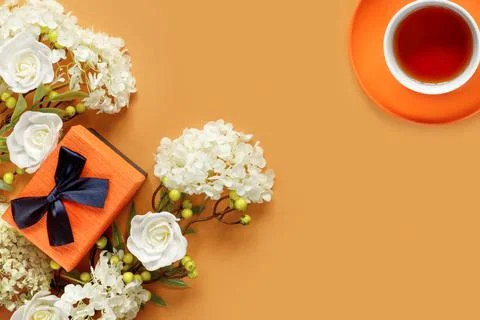 Gift box with white hydrangea and rose flowers on orange background. Cup of h Foto stock