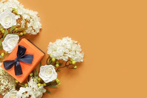 Gift box with white hydrangea and rose flowers on orange paper background. Co Stock Photos
