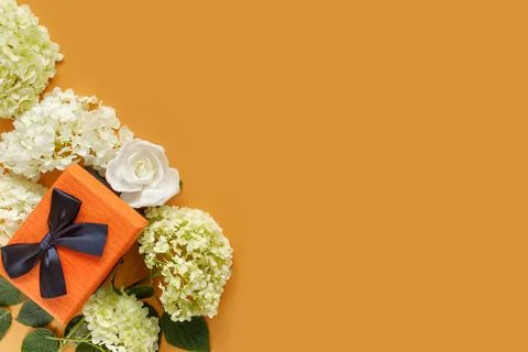 Gift box with white hydrangea and rose flowers on orange paper background. .. Foto stock