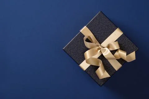 Gift box wrapped in dark blue paper with gold satin ribbon on a dark blue b.. Foto stock