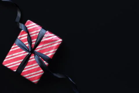 Gift box wrapped in red striped paper and tied with black bow Stock Photos