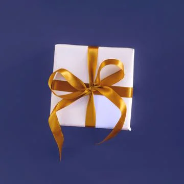 Gift box wrapped in white paper with a golden bow on festive violet blue Stock Photos