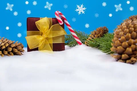 Gift box with yellow bow, candy cane and cones with fir branches on snow Stock Photos