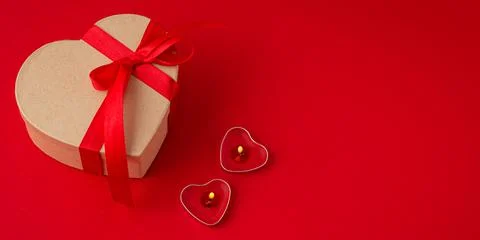 Gift boxe in heart shape with bow and two candles on red background, Saint Stock Photos