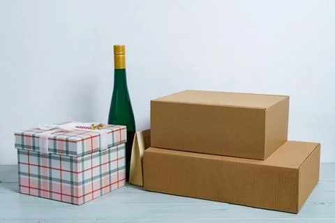Gift boxes and a bottle of wine on a light table on a white background. Stock Photos