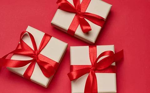 Gift boxes in beige packaging with red satin bows on a bright red background Stock Photos