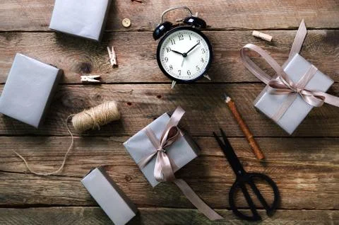 Gift boxes, black alarm clock, pen, scissors on wooden background. Preparing for Stock Photos