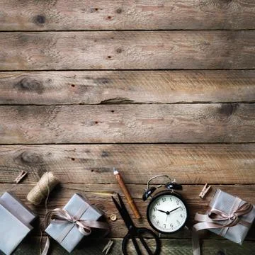 Gift boxes, black alarm clock, pen, scissors on wooden background. Preparing for Фото