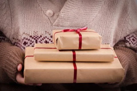 Gift boxes with red ribbon in the hands. Hands hold gifts in craft paper Stock Photos