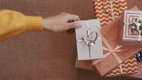 Gift boxes wrapped in gift paper. The girl puts one present on top. Top View Stock Footage 220770766