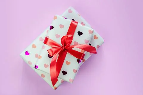 Gift boxes wrapped in heart pattern paper with red ribbon bow on pink background Stock Photos
