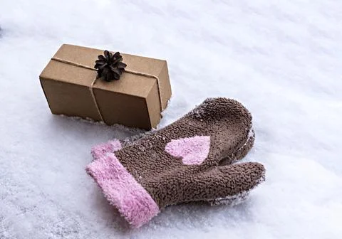 Gift in a craft box decorated with pine cone on white snow and mittens heart Stock Photos