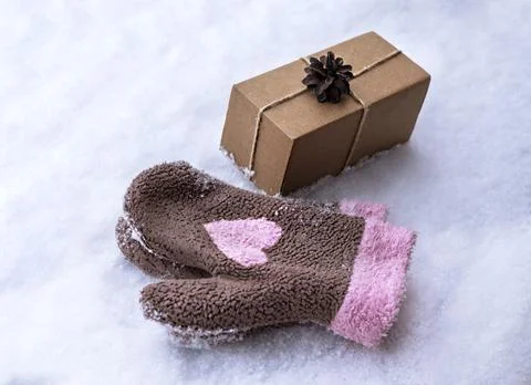Gift in a craft box decorated with pine cone on snow and mittens pink heart Stock Photos