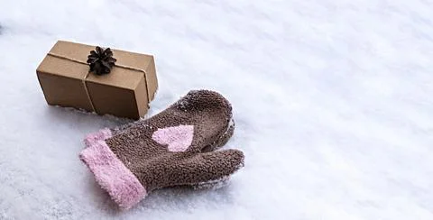 Gift in a craft box decorated with pine cone on white snow and mittens with p Stock Photos