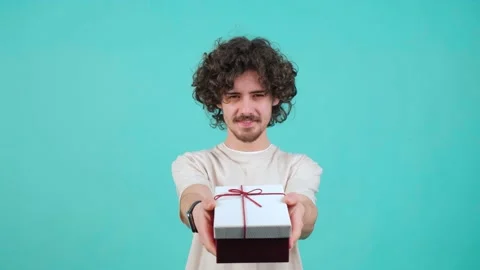 Gift delivery. Smiling curly haired man offering wrapped box to camera. Stock Footage 150960247