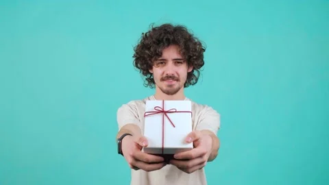Gift delivery. Smiling curly haired man offering wrapped box to camera. Stock Footage 153108548