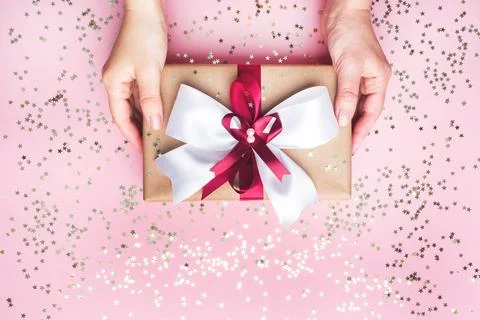 Gift or present box with a big bow in the hands of a woman on a pink table... Stock-Fotos