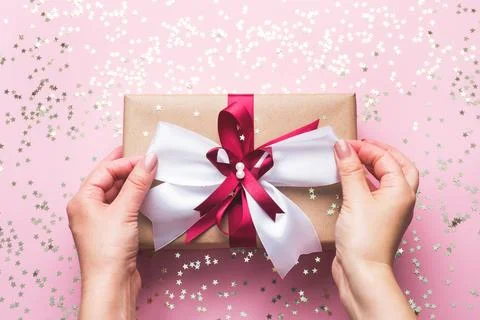 Gift or present box with a big bow in the hands of a woman on a pink table... 스톡 사진