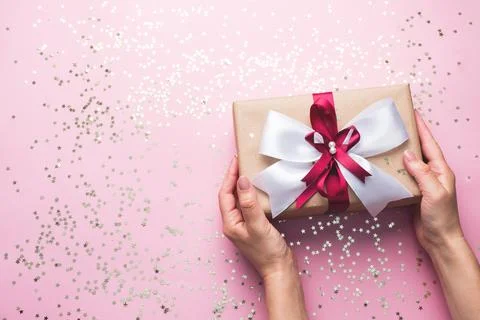 Gift or present box with a big bow in the hands of a woman on a pink table... 스톡 사진