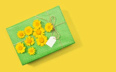 Gift or present box with blank label and daisy flowers on yellow background.. Stock Photos