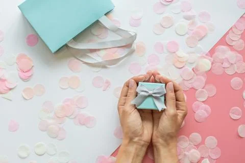 Gift or present box, hands and confetti on pink table top view. Flat lay comp Stock Photos