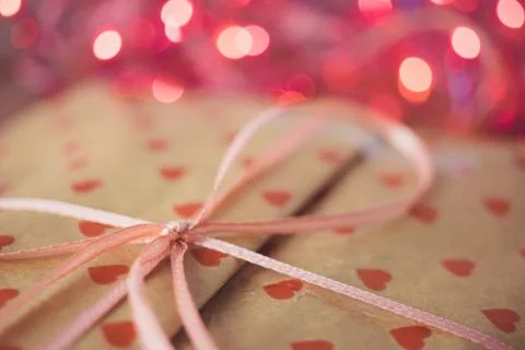 Gift in paper packaging with a pattern of red hearts, ribbon bow and pink lig Stock Photos