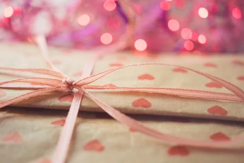 Gift in paper packaging with a pattern of red hearts. Ribbon bow and pink lig Stock Photos