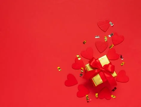 Gift with a red bow on a red background with glitter hearts and confetti Stock Photos