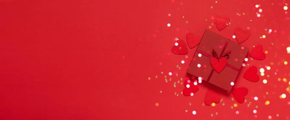 Gift with a red bow on a red background with glitter hearts and confetti Stock Photos