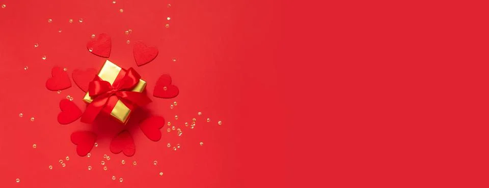 Gift with a red bow on a red background with glitter hearts and confetti Stock Photos